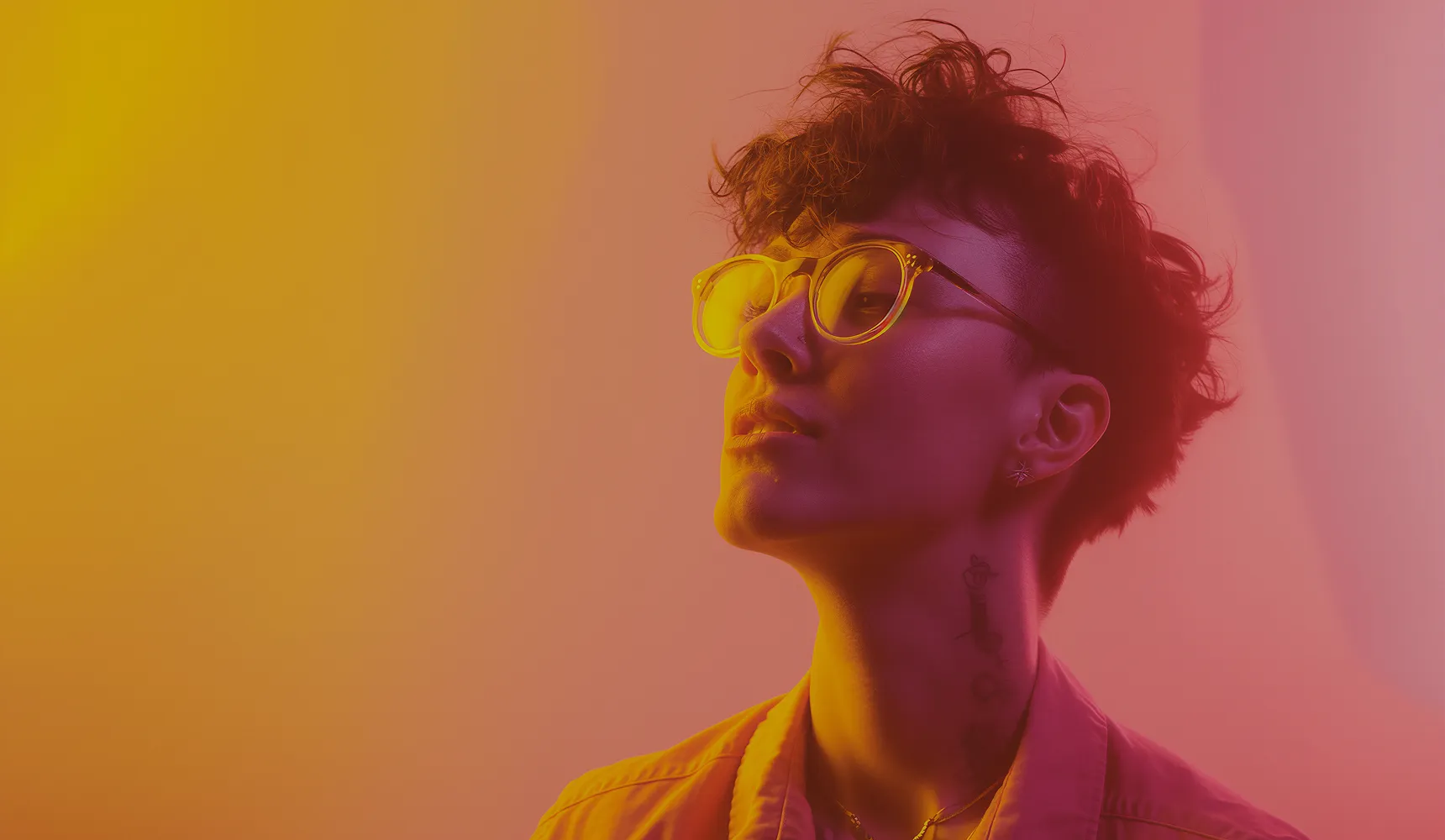 Persona de pelo corto y rizado con gafas mirando hacia arriba sobre un fondo degradado naranja y rosa.